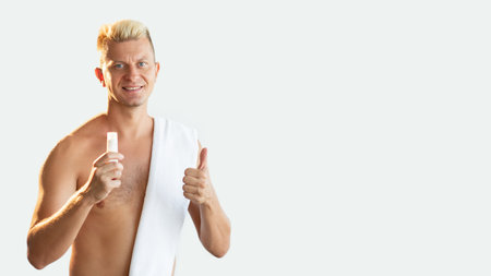 Male skincare. Advertising background. Perfect choice. Satisfied shirtless athletic blond man showing small white tube with lotion or cream approving with thumb up isolated on light empty space.の写真素材