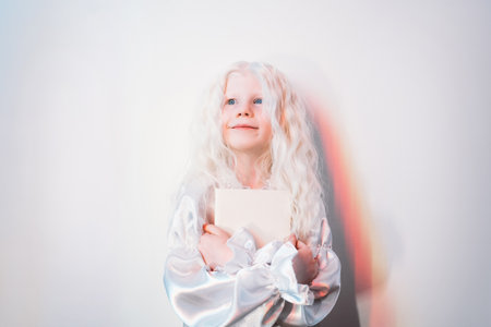 Kid dream. Happy childhood. Imagination freedom. Portrait of inspired sweet blonde little girl with curly hair in white vintage dress creating story in mind on light copy space background.の写真素材