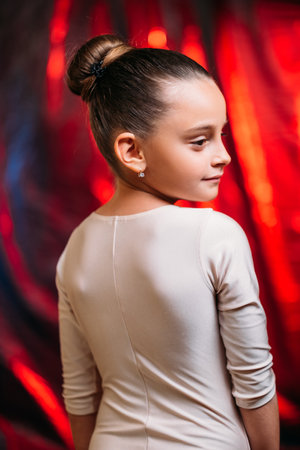 Little ballerina lifestyle. Child sport. Gymnastics class. Back view portrait of happy small girl in white bodysuit posing on red glow wrinkled texture background.の写真素材