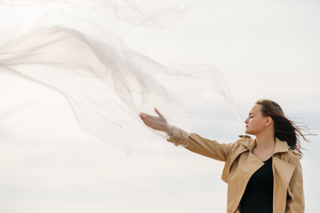 Woman confidence. Feminist empowerment. Freedom independence. Portrait of peaceful lady in beige trench coat with flying away hair enjoying wind energy with closed eyes on cloudy autumn sky.の写真素材