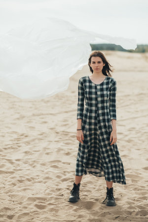 Woman independence. Feminist empowerment. Hope inspiration. Confident lady in check dress standing in autumn wind sandy desert with flying polyethylene film in cloudy skyline.の写真素材