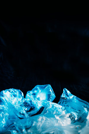 Ocean pollution. Ecology problem. Nature conservation. Waste reduction. Blue abstract ice water from wrinkled texture transparent cellophane bag isolated on dark empty space background.の写真素材