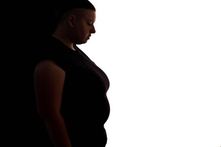 Obesity problem. Fat liposuction. Weight loss. Profile portrait of ashamed upset chubby woman body silhouette with big abdomen isolated on contrast white black copy space background.の写真素材