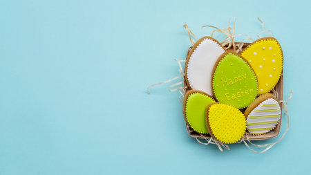 Happy Easter. Festive composition. Holiday bakery food. Greeting card. Colorful arrangement of green yellow white gingerbread biscuit egg set in rustic basket isolated on blue copy space background.の写真素材