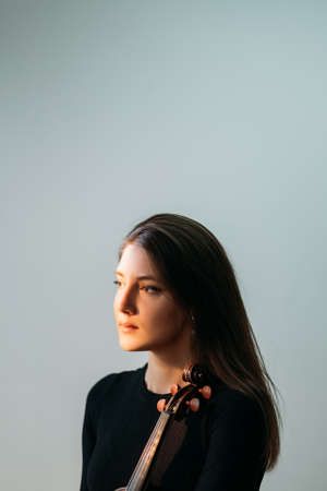 Female violinist portrait. Musician artist. Hobby amusement. Professional photo session. Beautiful woman posing with violin isolated gray warm spot light.の写真素材