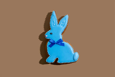 Happy easter. Gingerbread bunny. Festive bakery. Spring holiday celebration. Sweet animal figure cookie with blue icing decoration isolated on beige copy space.の写真素材