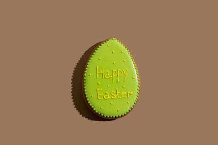 Happy easter bakery. Handmade gingerbread. Festive decoration. Sweet cookie egg with green icing and holiday wish text isolated on beige copy space.の写真素材