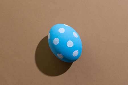 Easter egg. Festive gift card. Spring holiday. Abstract background. Blue paschal symbol with white spotted ornament pattern isolated on beige copy space.の写真素材