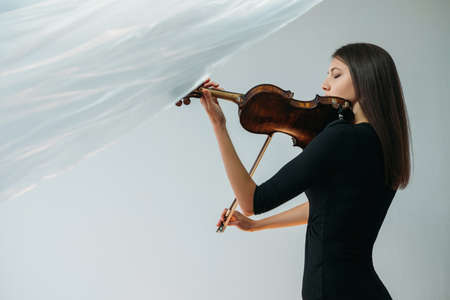 Musician woman. Online concert. Lockdown reality. Hobby profession. Creativity freedom. Inspired lady playing violin with transparent plastic film under head isolated neutral copy space.の写真素材