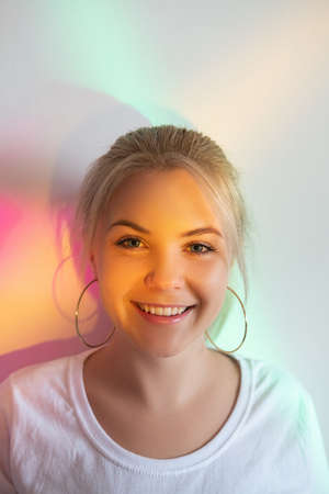 Happy woman. Dental health care. Beauty treatment. Smiling blonde lady with smooth skin looking at camera isolated on white blur rainbow glowing neon lights background.の写真素材