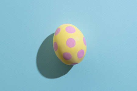 Easter egg. Festive decoration. Gift card. Spring holiday. Abstract background. Yellow paschal symbol with pink spotted ornament pattern isolated on blue textured copy space.の写真素材
