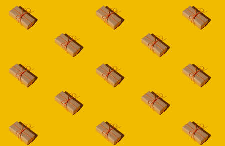 Gift pattern. Yellow seamless background. Holiday sale. Long-distance present collection. Minimalist diagonal composition of rustic beige handmade paper boxes with twine isolated on bright orange.の写真素材