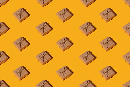 Gift pattern. Orange seamless background. Vintage mail parcel. Holiday congratulation. Symmetrical composition of rustic beige handmade paper boxes with twine isolated on bright yellow.の写真素材