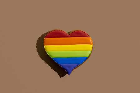 Heart gingerbread cookie with rainbow icing decoration isolated on beige.