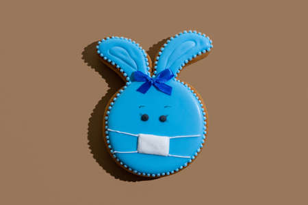 Bunny gingerbread cookie with blue icing and protective mask ornament isolated on beige.