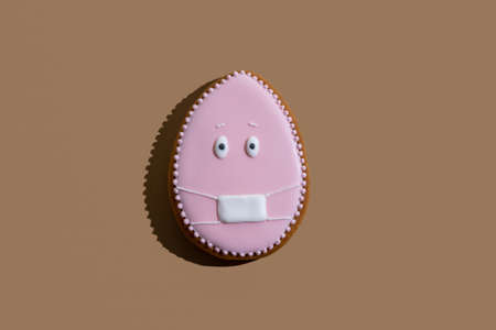 Pretty egg gingerbread cookie with pink icing and medicine mask ornament isolated on beige.
