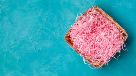 Handmade gift package. Festive banner. Eco decor. Empty wooden basket box with pink straw composition for food present delivery on blue painted textured copy space background.の写真素材