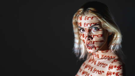 Conceptual female portrait. Program failure. Hacker attack. Computer bug. Wrong data. Scared woman with red inscription error on face body isolated on dark copy space double exposure.の写真素材