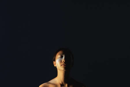 Ethnic portrait. Tribal beauty. Wild spirit. Relaxed peaceful inspired native Indian woman with closed eyes bare shoulders painted face isolated on black copy space background.の写真素材