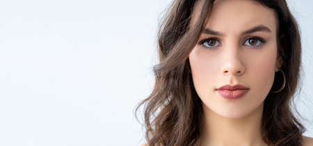 Beauty portrait. Facial skincare. Aesthetic cosmetology. Brunette woman with perfect smooth face full lips looking at camera isolated on white copy space advertising background.の写真素材