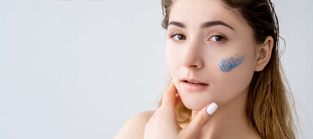 Skincare banner. Facial peeling. Acne treatment. Portrait of confident woman with natural makeup flawless face with blue beads gel scrub cleanser stroke isolated on neutral empty space background.の写真素材