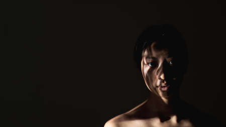 Female rights. Gender discrimination. Safety protection. Art portrait of insecure woman silhouette with abstract shadow pattern on face bare shoulders isolated on black night copy space background.の写真素材