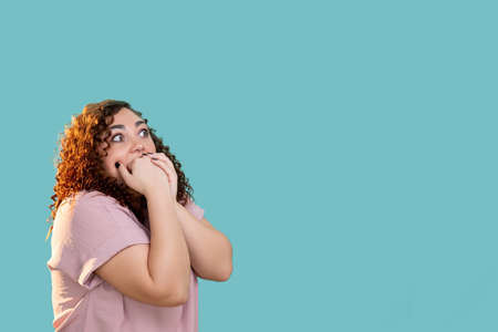 Shocked woman. Diet problem. Overweight struggle. Body positive lifestyle. Information banner. Scared plus size lady biting hand fists looking copy space isolated blue.の写真素材