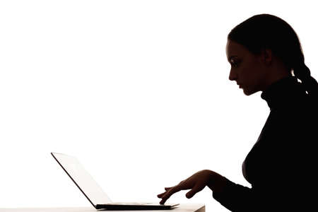 Woman silhouette. Online learning. Distance education. Dark contrast profile shape portrait of smart female student working with laptop in virtual class isolated on white empty space background.の写真素材