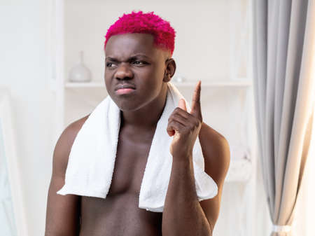 Guess idea. Funny black man. Morning grooming. Skincare treatment. Eureka gesture. Thoughtful shirtless african guy with bright pink hair holding finger up in bathroom interior.の写真素材