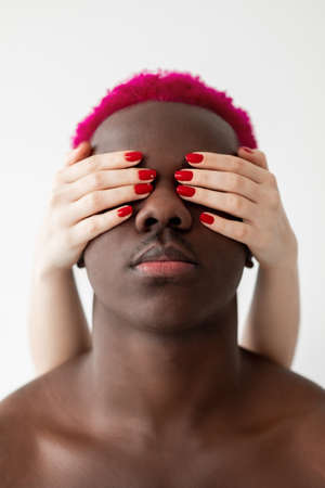 Racial tolerance. Blind man. Black lives matter. Couple support. Multiethnic relationship. Conceptual art portrait. White female hand closing eyes african guy pink hair isolated light.の写真素材