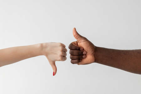 Like dislike gesture. Racial tolerance. Versus opposition. Gender diversity. Problem cooperation. Conceptual art. White female and black male hands showing thumbs up down isolated light.の写真素材