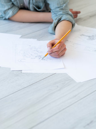 Drawing art. Creative hobby. Graphic design. Craft skill. Left-handed woman artist sketching with pencil on white paper on light wooden texture surface.の写真素材