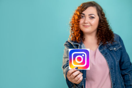 Kharkiv, Ukraine - November 06, 2020: Instagram icon. Mobile application. Social media. Sharing photo video. Smiling woman showing symbol logotype isolated blue copy space.のeditorial素材