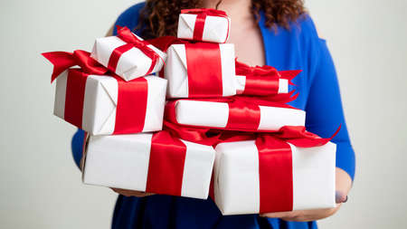 Holiday gift. Black friday. Surprise bonus. Fast delivery. Greeting celebration. Unrecognizable woman blue dress holding festive wrapped present boxes red tape isolated white.の写真素材