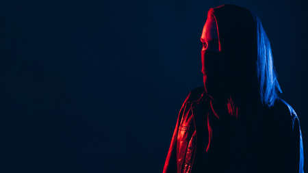 Activist portrait. Night riot. Cyberpunk banner. Revolution protest. Red blue neon light woman in black face bandana buff mask leather jacket isolated on dark copy space background.の写真素材