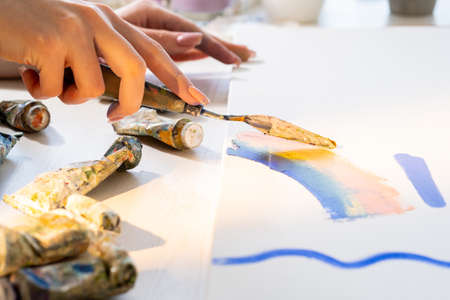Painting process. Abstract style. Artistic tools. Creative master class. Unrecognizable woman using palette knife for expressive artwork tube paints on table.の写真素材