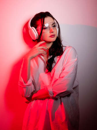 Music chill. Urban lifestyle. Futuristic technology. Relaxed red neon light girl in glasses enjoying listening mp3 sound in wireless headphones isolated on pink background.の写真素材
