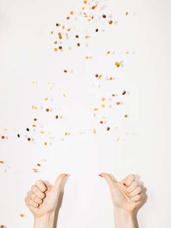 Like party. Festive invitation. Birthday celebration. Cool holiday. Advertising background. Female hands showing thumbs up with throwing golden confetti spangles isolated white copy space.の写真素材