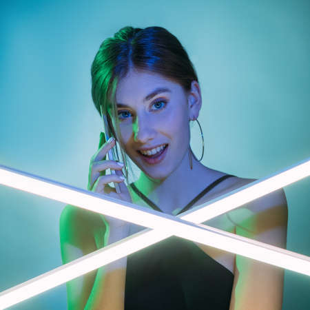 Phone call. Mobile communication. Futuristic technology. Green blue neon light surprised curious woman speaking using wireless gadget isolated on color gradient background.の写真素材
