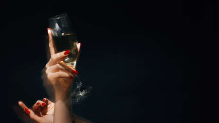 Party fun. Birthday celebration. Holiday spirit. Festive background. Female hands holding glass of champagne long exposure defocused light isolated black copy space.の写真素材