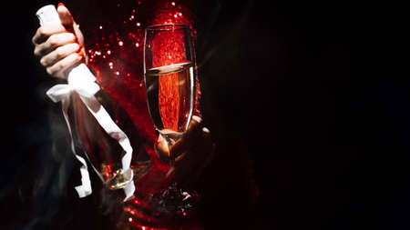 Festive background. Party fun. Holiday celebration. Unrecognizable woman red dress holding sparkle glass bottle of champagne long exposure defocused light on black copy space.の写真素材