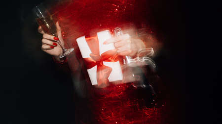 Party overdrink. Holiday fun. Birthday celebration. Festive joy. Unrecognizable woman red dress holding glass and bottle champagne gift box long exposure defocused light on black.の写真素材