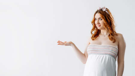 Baby shower party. Pregnant woman. Open palm. Important information. Advertising background. Pretty smiling tummy lady holding promoting hand isolated white copy space.の写真素材