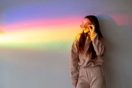 Neon street fashion. Modern youth. Urban style. Beautiful lovely girl in sunglasses side looking on blur rainbow color rays copy space background.の写真素材