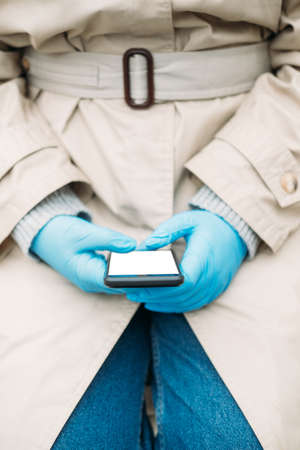Woman hands in medical gloves typing on white blank screen smartphone display.