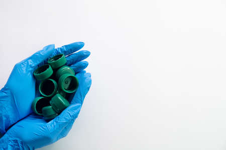 Ecology problem. Global pollution. Save planet. Volunteer hands in medical gloves holding green plastic bottle caps isolated on white copy space background.の写真素材