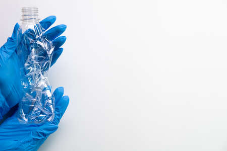 Ecology volunteering. Plastic utilization. Environment concern. Unrecognizable hands in medical gloves holding used crushed bottle isolated on white copy space background.の写真素材
