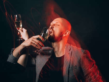 Birthday party. Brotherhood drink. Holiday fun. Festive celebration. Stylish man drinking glass of champagne with unrecognizable woman isolated black long exposure defocused red light.の写真素材