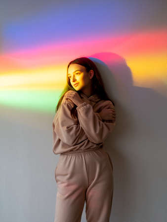 Color light people. Self love. Calm energy. Feel good. Peaceful relaxed girl hugging self on smooth blurred rainbow neon glow wall.の写真素材