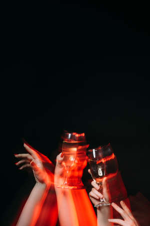 Birthday party. Friends celebration. Holiday fun. Festive overdrink. Female hands holding glasses of champagne long exposure defocused red light isolated black copy space.の写真素材